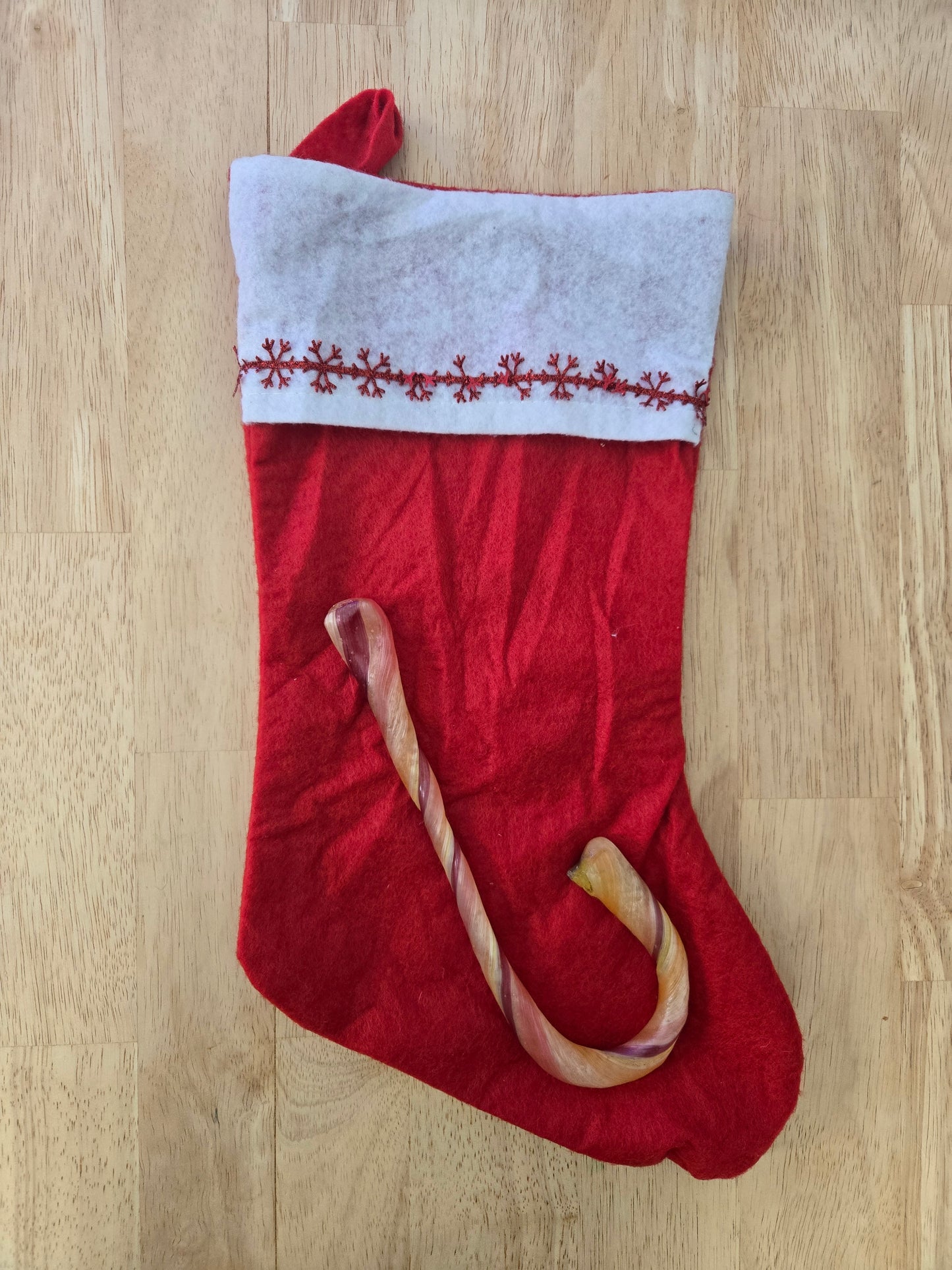 Red Christmas stocking with white cuff and giant natural dye free candy cane on a wooden floor