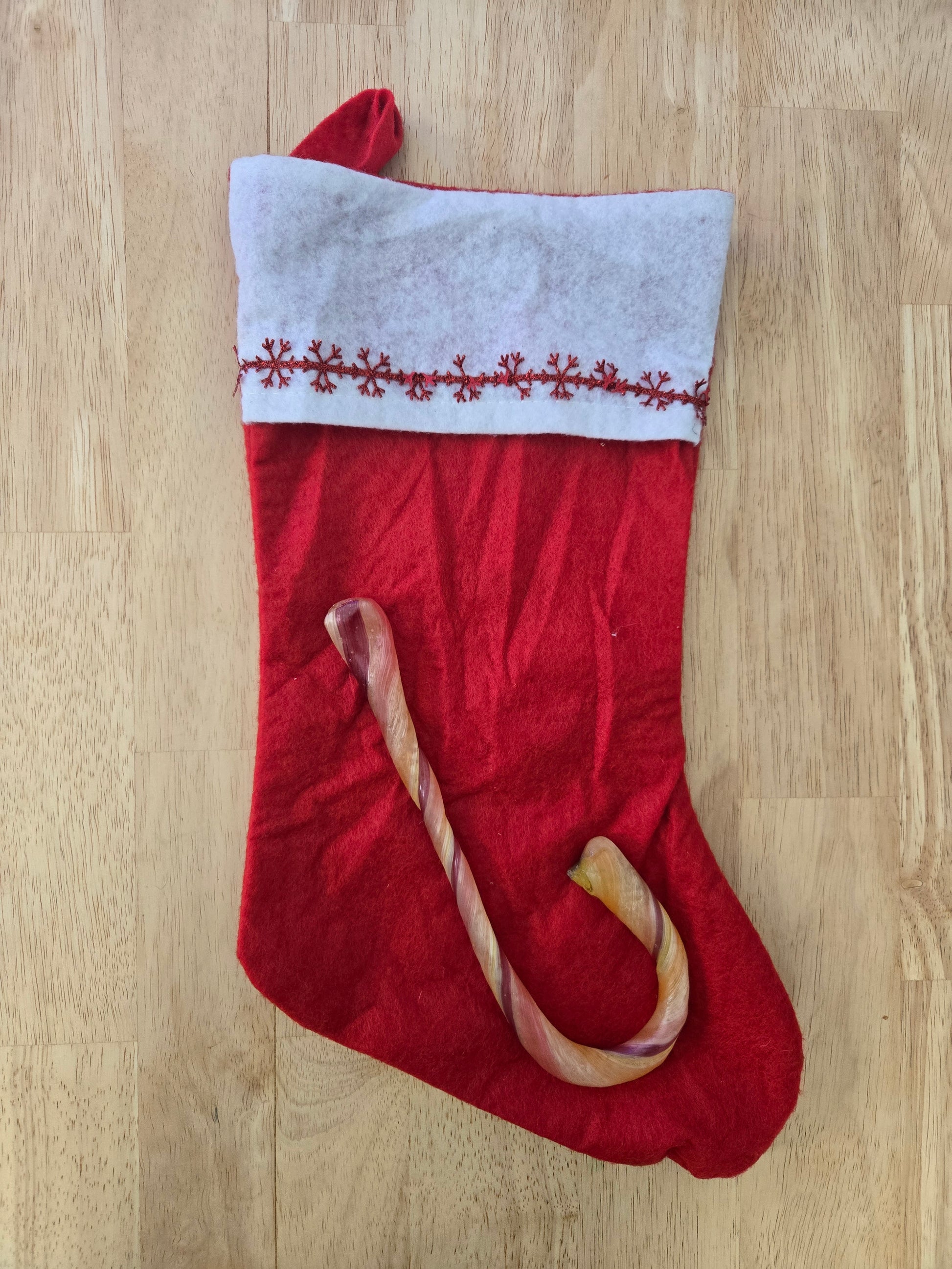 Red Christmas stocking with white cuff and giant natural dye free candy cane on a wooden floor