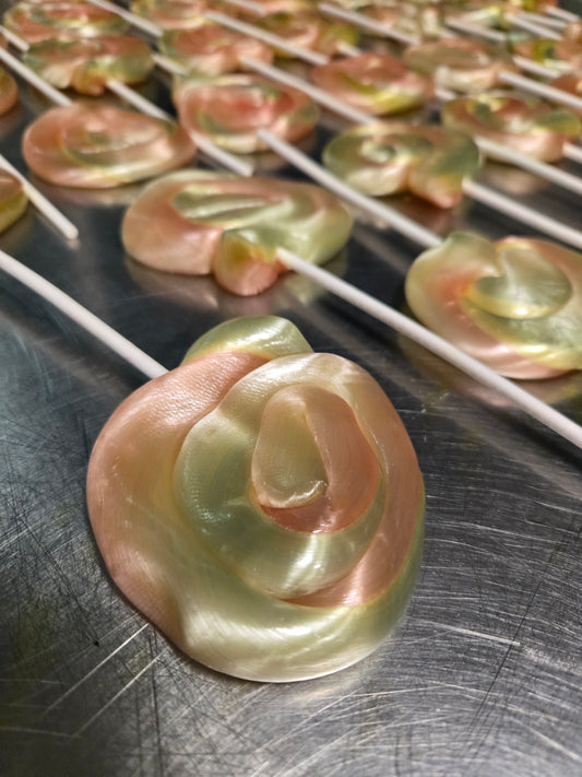 Decorative dye free pink and green swirl lollipops on a cooling rack with a metal surface below