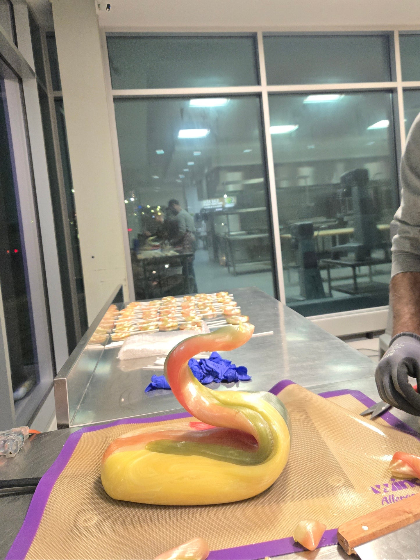 Person working on a  hand made lollipop with a big piece of sugar and window reflections.